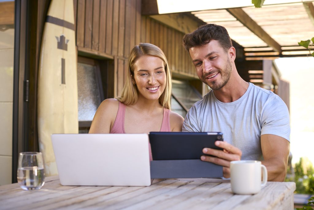 Couple With Laptop And Digital Tablet Outdoors On Table At Home