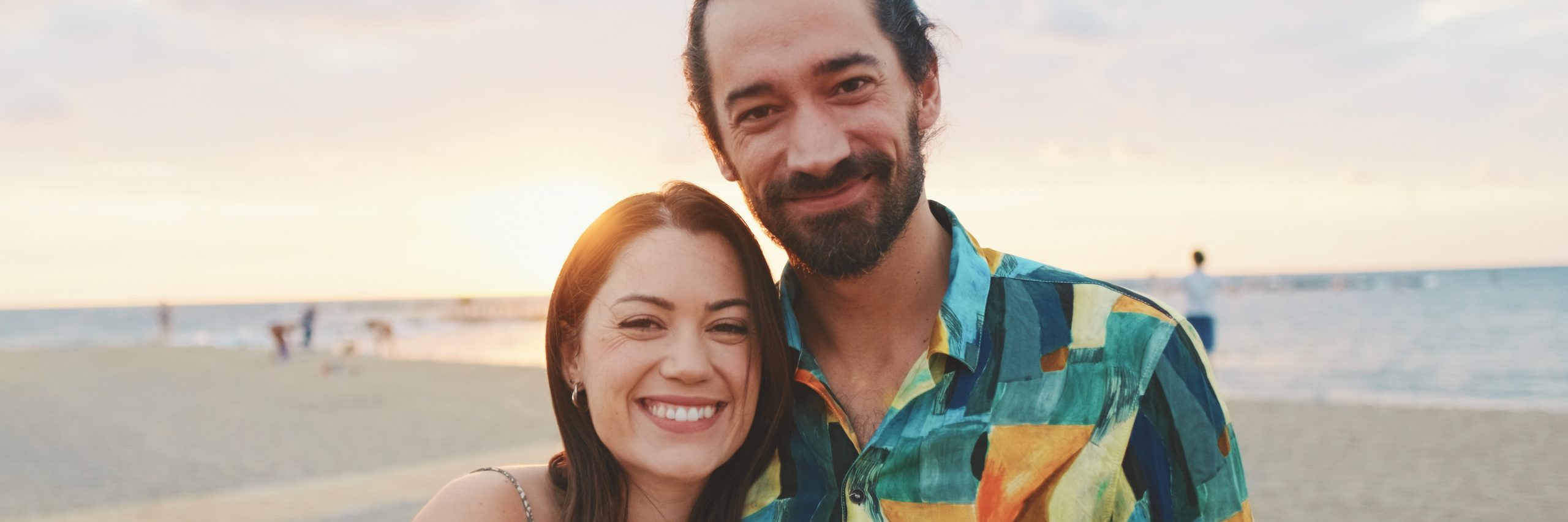 Young couple standing on the beach at sunrise, panorama