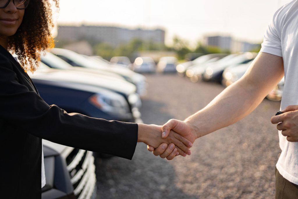 Handshake between two people at a car dealership representing a novated lease calculator used to compare vehicle cost scenarios