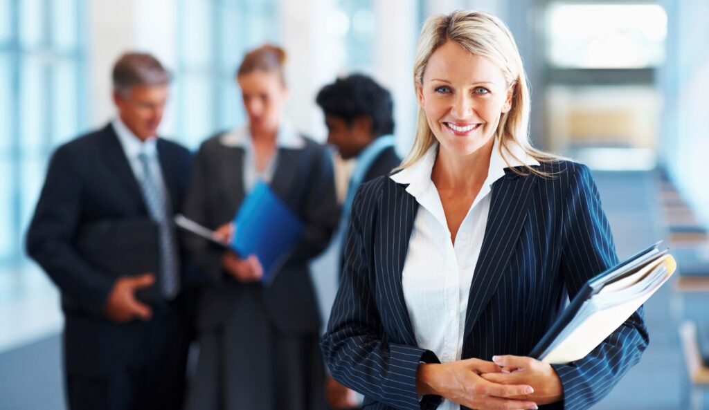 Queensland Health professional smiling confidently in an office while holding salary packaging documents, with colleagues discussing benefits and financial options in the background. qld health salary packaging